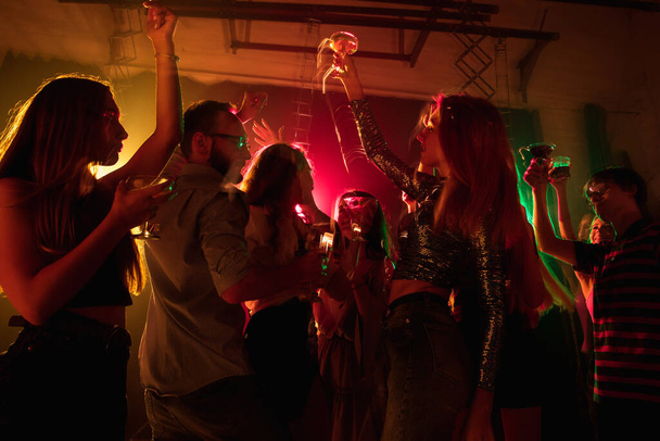 Una multitud de personas en silueta levanta sus manos en la pista de baile sobre fondo de luz de neón - Foto, imagen