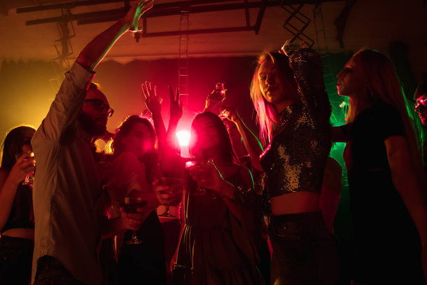 A crowd of people in silhouette raises their hands on dancefloor on neon light background - Foto, Bild