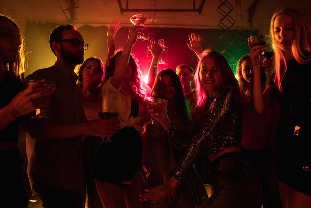 A crowd of people in silhouette raises their hands on dancefloor on neon light background - Foto, imagen