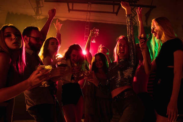 A crowd of people in silhouette raises their hands on dancefloor on neon light background - Foto, imagen