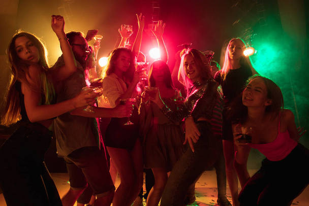 A crowd of people in silhouette raises their hands on dancefloor on neon light background - Fotoğraf, Görsel