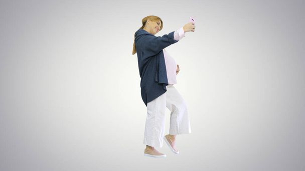 Happy young pregnant woman taking selfie on gradient background. - Fotografie, Obrázek
