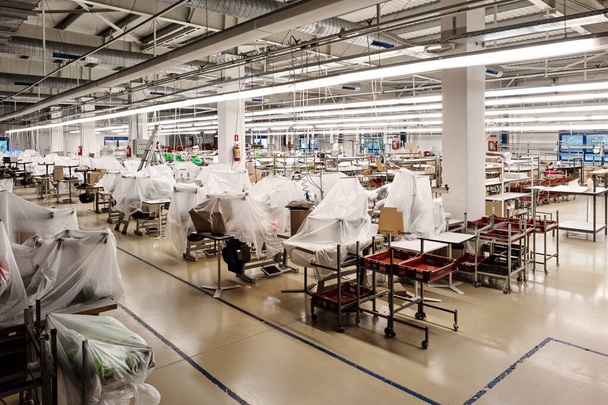 Small out of business garment factory production lines with groups of industrial sewing machines covered up in foil and carton. - Photo, Image
