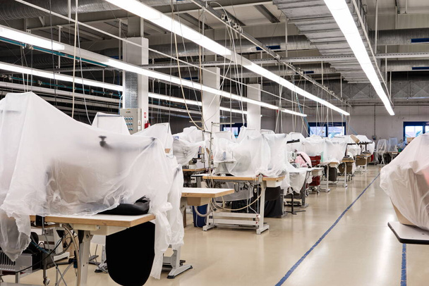 Kleinschalige productielijnen voor kledingfabrieken met groepen industriële naaimachines bedekt met folie en karton. - Foto, afbeelding
