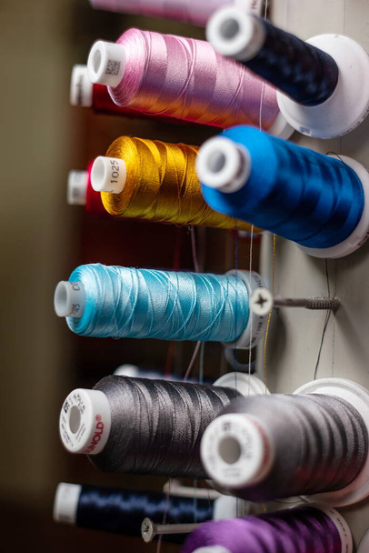 Carretes pequeños multicolor de pilas de hilo de coser en la pantalla del cilindro grande. - Foto, Imagen