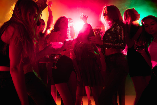 A crowd of people in silhouette raises their hands on dancefloor on neon light background - Fotoğraf, Görsel