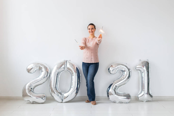 Celebración de Año Nuevo y concepto de fiesta - Mujer joven feliz con brillantes cerca de plata 2021 globos sobre fondo blanco. - Foto, imagen