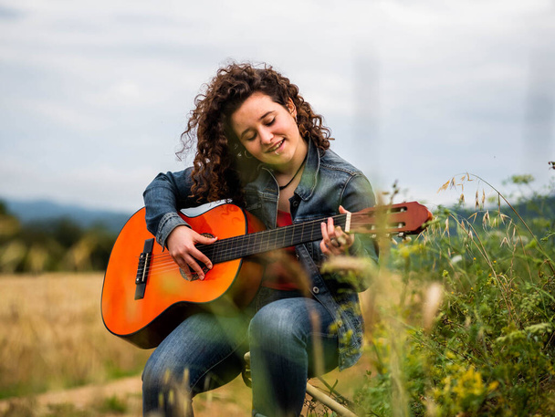 Buğday tarlasında gitar çalan genç ve güzel bir kadının sığ odak noktası. - Fotoğraf, Görsel