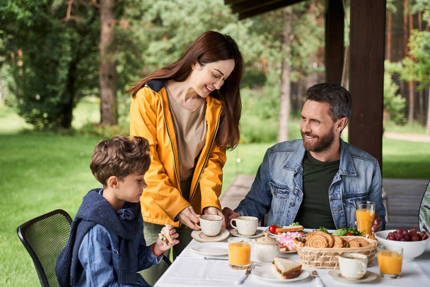 Cute boy having breakfast with parents outdoors - Photo, Image