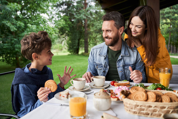Happy parents chatting with son while having breakfast outdoors - Foto, afbeelding