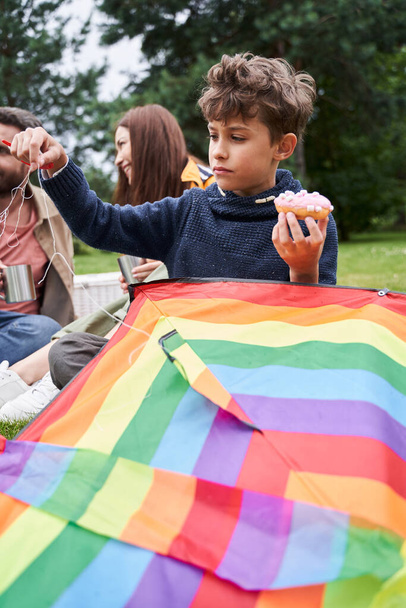 Cute boy playing with kite while having picnic with parents - Photo, image