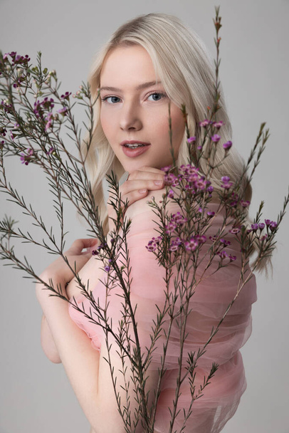 Charming young woman standing behind sprigs with tiny flowers - Fotografie, Obrázek