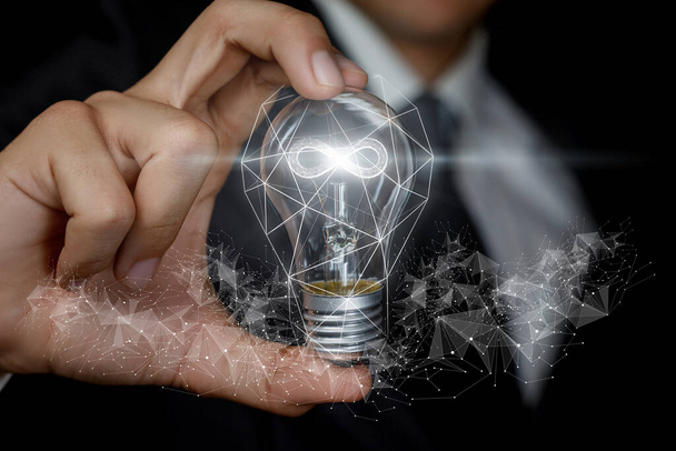 Concept d'idées d'affaires sans fin. La main montre une ampoule avec un hologramme brûlant d'infini à l'intérieur. - Photo, image