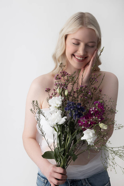 Radostná mladá žena s květinami stojí proti bílému pozadí - Fotografie, Obrázek