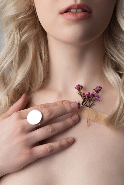 Blonde young woman touching band-aid with flower on her skin - Foto, Imagem