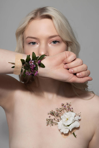 Pretty lady with flowers on her skin standing against gray background - Zdjęcie, obraz
