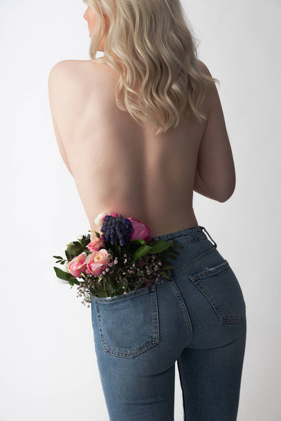 Slim young woman wearing blue jeans with flowers in pocket - Fotoğraf, Görsel