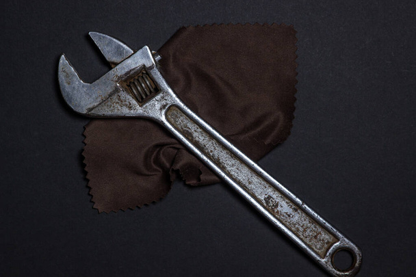 Working tools on a black background. Manual labor concept. The adjustable wrench lies on a brown rag - Photo, Image
