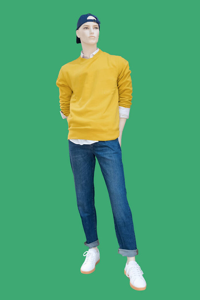 Полный мужской манекен, одетый в желтый свитер и синие джинсы, выделенный на зеленом фоне. Нет фирменных наименований или объектов авторского права. - Фото, изображение