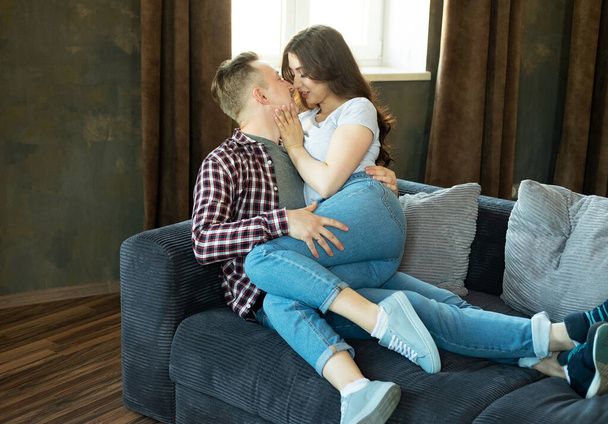 Young beautiful couple is sitting on the couch and hugging. Happy family life. - Foto, afbeelding