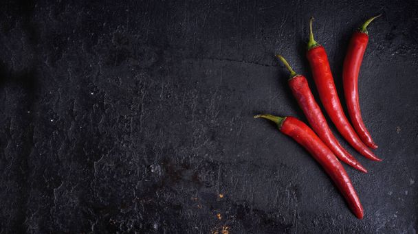 Red hot chili peppers on black rustic textured slate from above. Food background with spicy chilli paprika. Top view. - 写真・画像