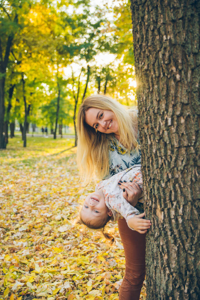 μητέρα με την κόρη τιτιβίζει από το δέντρο φθινόπωρο δημόσιο πάρκο - Φωτογραφία, εικόνα