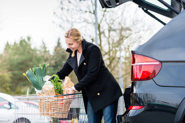 Женщина загружает продукты после покупки в багажник своей машины - Фото, изображение