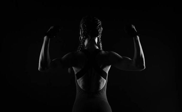 Een brutale atletische vrouw pronkt met haar spieren door het opheffen van haar armen. - Foto, afbeelding