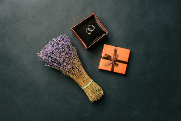 Kukkakimppu laventeli kukkia ja avoin lahjapaketti vihkisormukset mustalla taustalla. Häät tarvikkeet ja häät yksityiskohtia. Top view, tasainen asettelu - Valokuva, kuva
