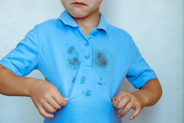 расстроенный мальчик показывает пятно на своей одежде концепция чистки пятен на одежде. Изолированный на белом фоне. Высокое качество фото - Фото, изображение