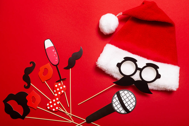 Una pancarta de color rojo con un sombrero de Santa Claus con un pompón blanco y una cara de gafas y bigote. Un accesorio para entretener a los invitados en una fiesta corporativa de Año Nuevo o una fiesta de karaoke para un equipo de barberos. - Foto, Imagen