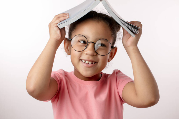 lauging kid is holding a book on her head - Foto, imagen