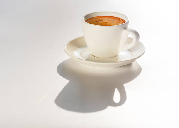 White cup of coffee on white background in natural morning sunlight. Copy space - Zdjęcie, obraz