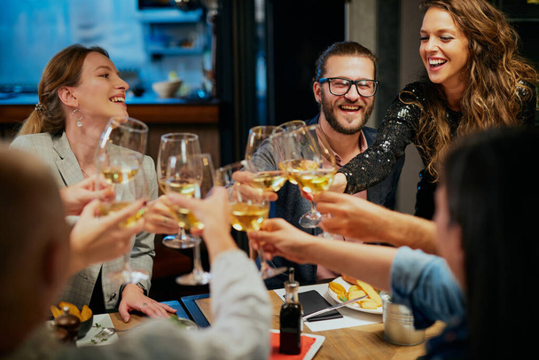Grupo de amigos celebrando en restaurante y brindando con vino blanco. - Foto, imagen