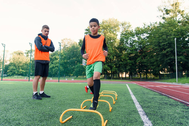 Motivated teen soccer players perform run exercises with overcoming obstacles applying racks on artificial soccer field. - Photo, Image