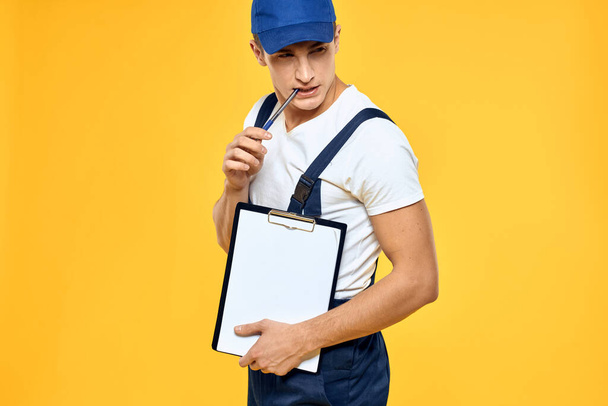 Man in het werken uniforme documenten weergave van diensten bezorgdienst gele achtergrond - Foto, afbeelding