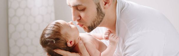 Fathers Day holiday. Happy Caucasian father kissing newborn baby. Dad man parent holding child daughter son on hands. Authentic lifestyle candid family moment. We banner header.  - Photo, Image