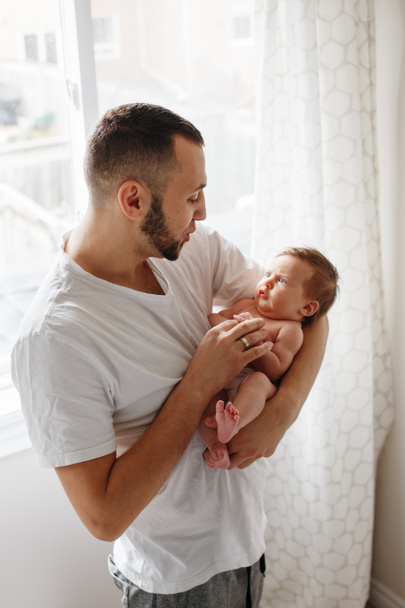 Boldog kaukázusi apa újszülött babával a kezében. Férfi szülő ringatózik, és a kislányával beszélget. Hiteles életstílus őszinte pillanat. Apák napja ünnep. - Fotó, kép