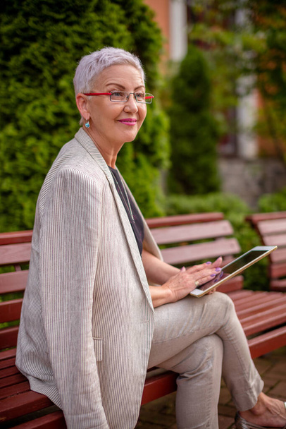 smiling woman is checking a new tablet while resting in the park - Photo, image