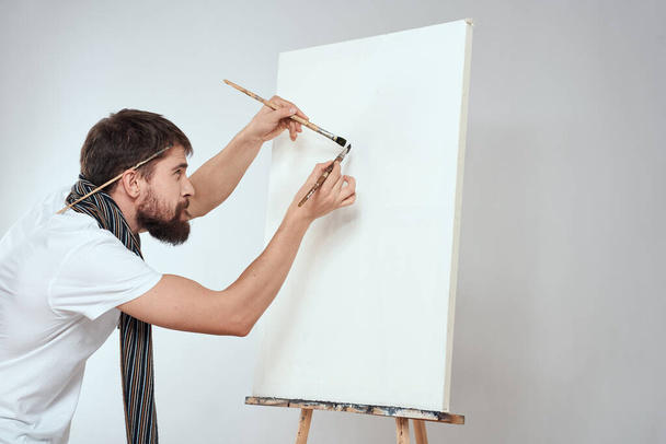 Чоловічий художник пензлик в руках мольберта хобі легкий фон шарф на шиї
 - Фото, зображення