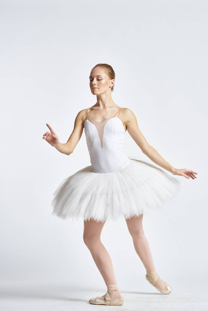 Ballerina in a white tutu performing dance exercise flexibility light background - Photo, image
