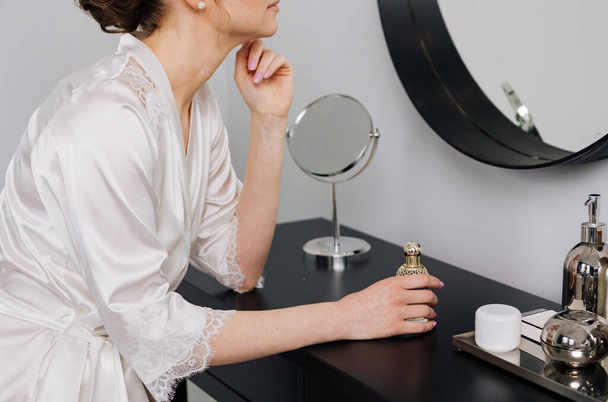 vrouw in zijde badjas in de voorkant van kleedkamer spiegel met accessoires - Foto, afbeelding