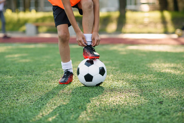 Close up boot of football player which puts his leg on ball and tying shoelace on soccer stadium on the training. - Photo, image