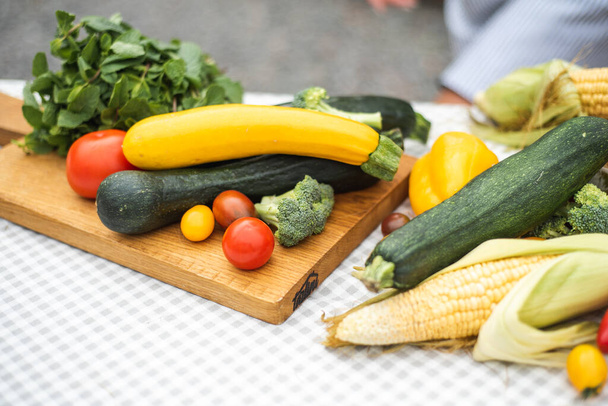 Летний урожай лежит на столе. Много овощей: цуккини, брокколи, помидоры, кукуруза, зелень. Высокое качество фото - Фото, изображение