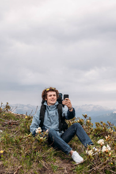cheerful backpacker is shootting the video while sitting on the hill - Фото, зображення
