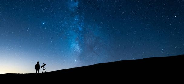 Geceleri mavi yıldızlı gökyüzünü teleskopla izleyen kişi. Evrenin ve Samanyolu 'nun büyüklüğünü gözlemleyen bir astronomun silueti. - Fotoğraf, Görsel
