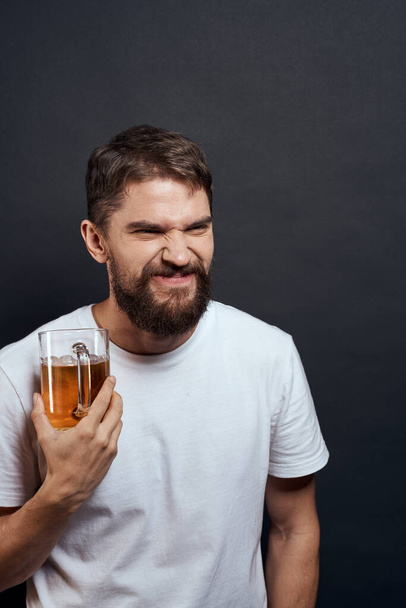 Férfi egy korsó sör a kezében érzelmek szórakoztató életmód fehér póló sötét elszigetelt háttér - Fotó, kép