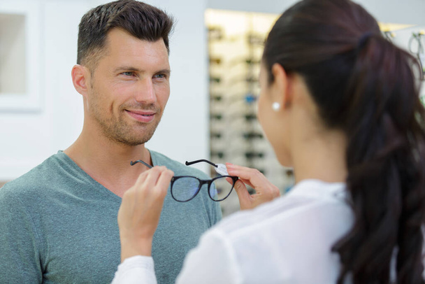 optician fitting glasses onto handsome male customer - Foto, afbeelding