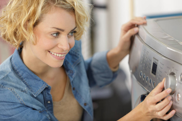 young happy woman using washing machine in utility room - 写真・画像