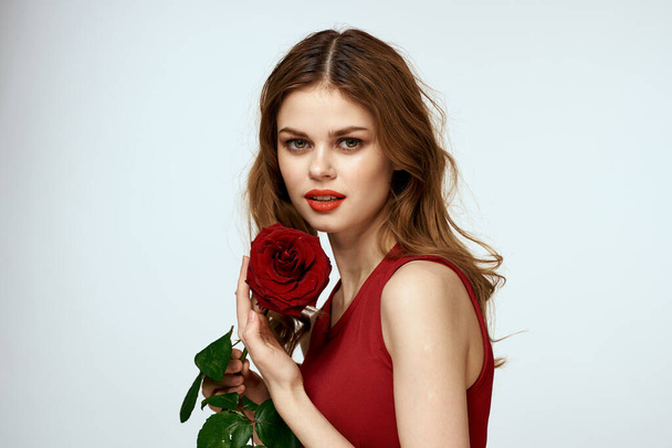 Krásná žena v červených šatech drží růži v ruce dárek květiny dekorace atraktivní vzhled - Fotografie, Obrázek